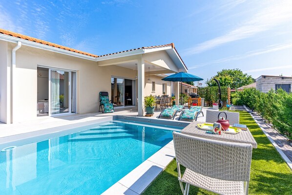 A swimming pool with a covered patio area, outdoor furniture, and a well-maintained lawn.
