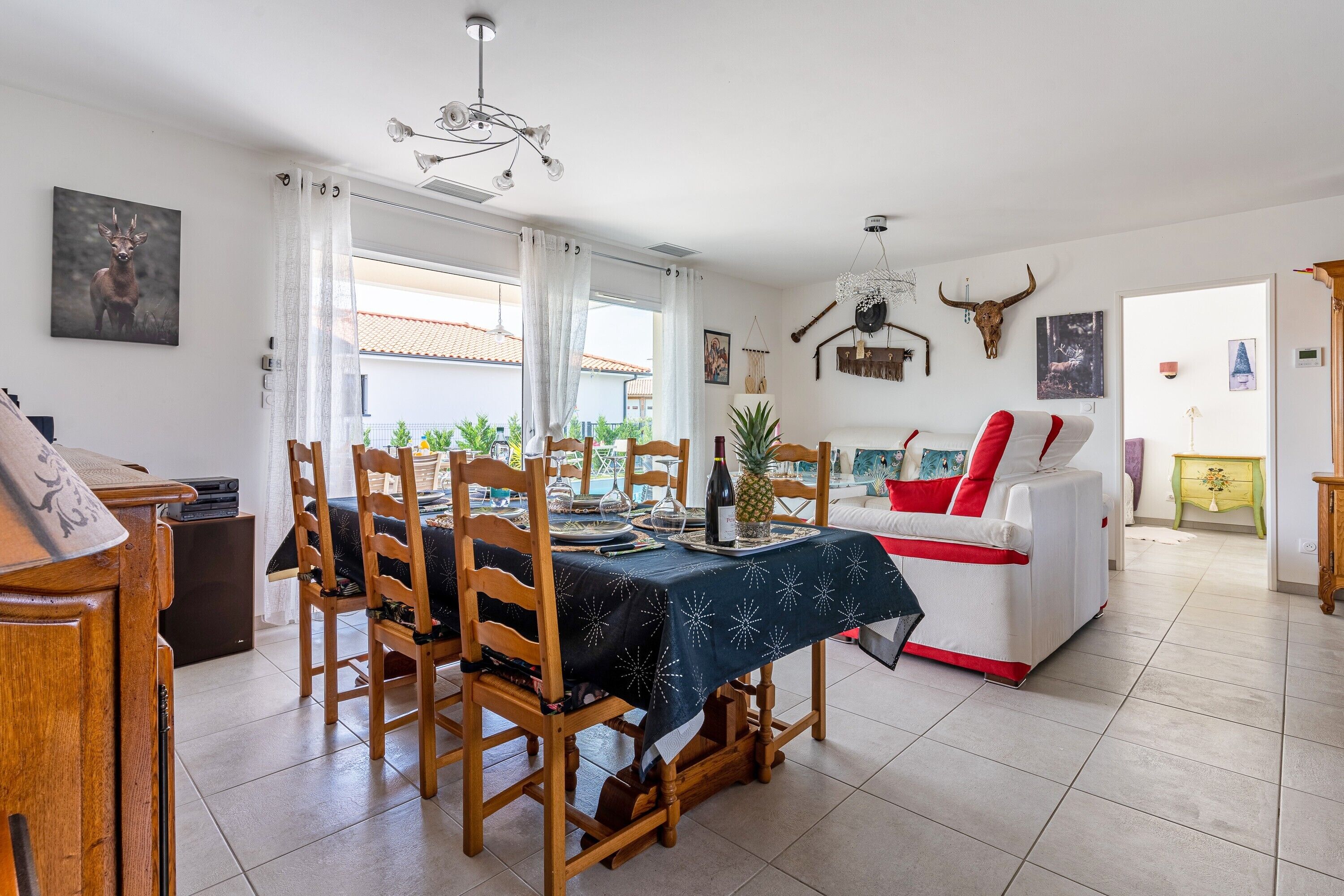 A dining area with a table set for four, wooden chairs, a chandelier, and a bull's head decoration on the wall.