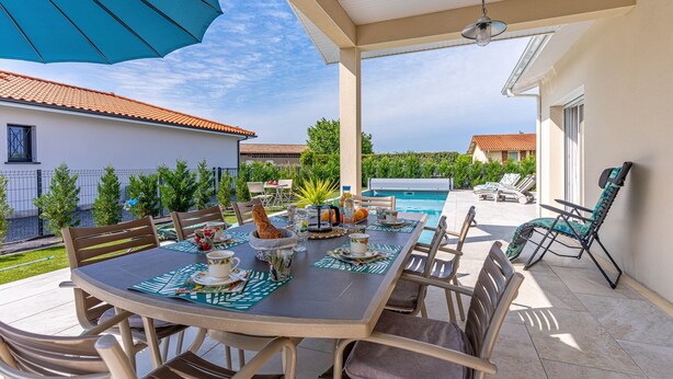 An outdoor patio with a dining table set for four, surrounded by chairs, a pool, and a covered area with a ceiling fan. - Beautiful Villa 500 m from the Lake with Pool and Air Conditioning (Gastes)