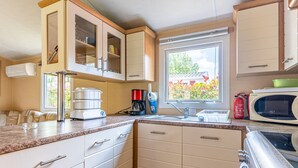 Cocina compacta con electrodomésticos integrados, ventana con vistas y encimera con cafetera y otros objetos.