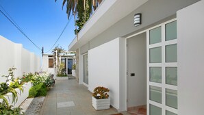 A narrow, clean pathway leading to a white building with a glass door, surrounded by greenery and a tiled floor. - Vacation Home "Paraíso" with Sea View, Pool & Wi-Fi (Puerto de la cruz)