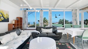 A living room with a sofa, a table, and a view of the outdoors. - Vacation Home "Paraíso" with Sea View, Pool & Wi-Fi (Puerto de la cruz)