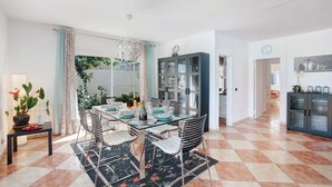 A dining area with a glass table, chairs, and a chandelier. There is a kitchen area with cabinets and a clock on the wall. - Vacation Home "Paraíso" with Sea View, Pool & Wi-Fi (Puerto de la cruz)