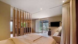 Une chambre moderne avec un grand lit, un téléviseur fixé au mur et un balcon équipé d’une table et de chaises.