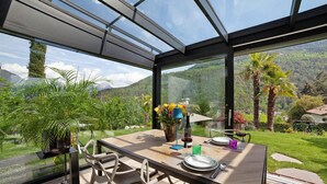 Un coin repas comprenant une table, des chaises, un vase avec des fleurs, une bouteille de vin et un verre.
