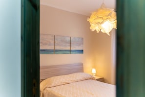 A bedroom with a bed, a nightstand, a wall-mounted lamp, and a painting of the sea. - Apartment 'Casamorle' with Private Terrace and Air Conditioning (Isola Rossa)