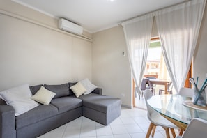 Una sala moderna con un sofá seccional gris, una mesa de comedor de vidrio y vistas al exterior.