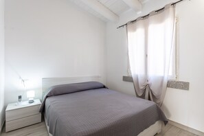 A bedroom with a bed, nightstand, and a window with curtains.