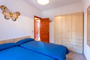 A bedroom with two beds, a wooden wardrobe, and a butterfly wall decoration.