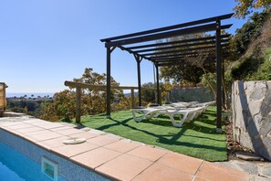 Zona de piscina con pérgola, sillas de descanso y vistas al paisaje.