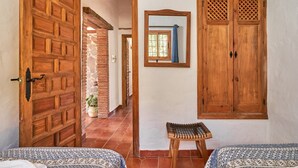 A room with a wooden door, a mirror, a bench, and a bed with patterned bedding. - Country House 'La Solana' with Sea View, Private Pool and Wi-Fi (Frigiliana)