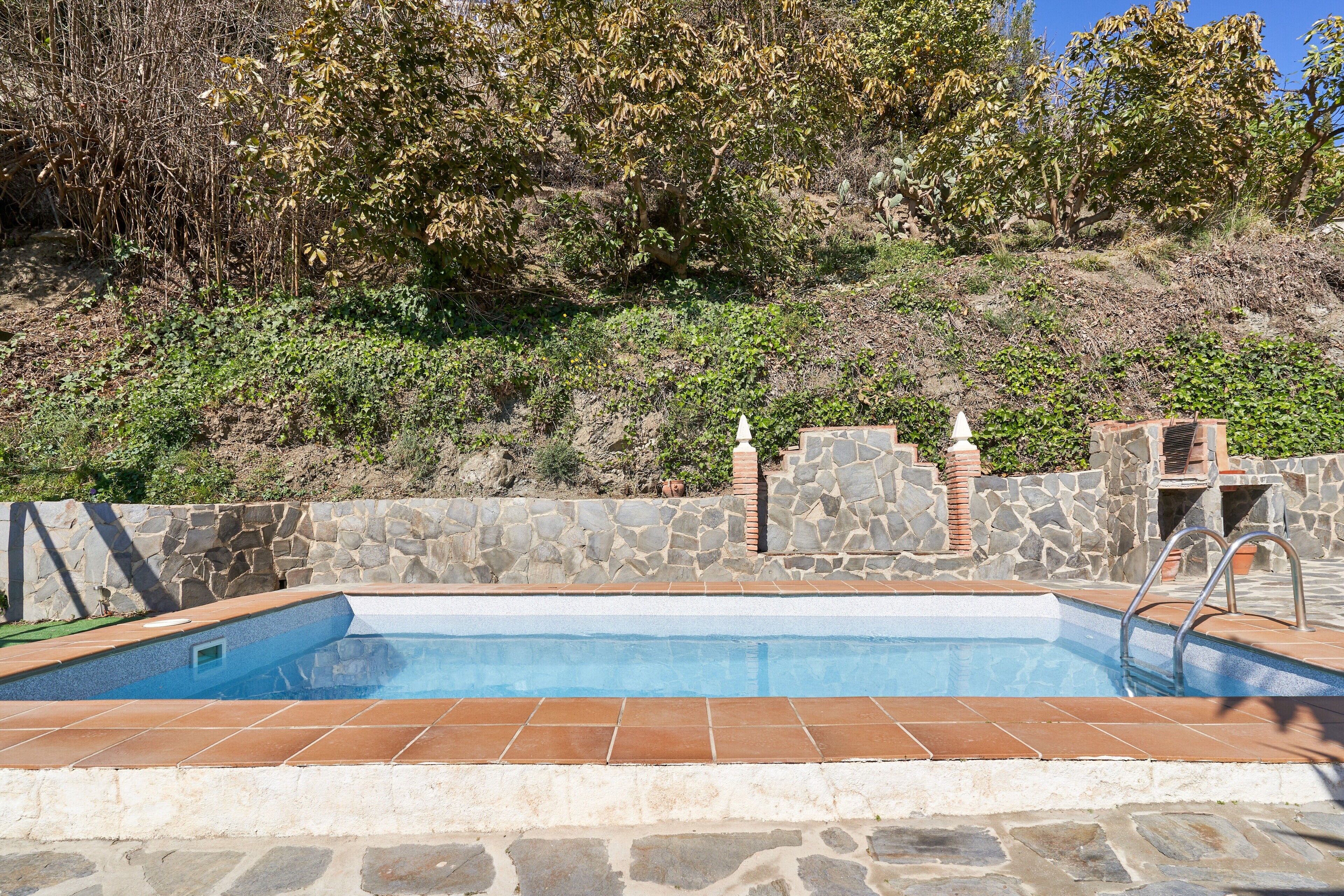 Una piscina con paredes de piedra y una escalera de piedra que sube a un patio.