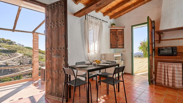 A dining area with a table set for four, a wooden door, and a view of a hilly landscape. - Country House 'La Solana' with Sea View, Private Pool and Wi-Fi (Frigiliana)