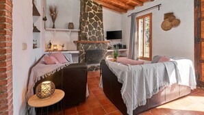 A cozy living room with a stone fireplace, wooden ceiling beams, and a television mounted on the wall. - Country House 'La Solana' with Sea View, Private Pool and Wi-Fi (Frigiliana)