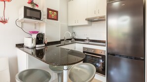 A modern kitchen with a black countertop, white cabinets, a stainless steel refrigerator, and a microwave.