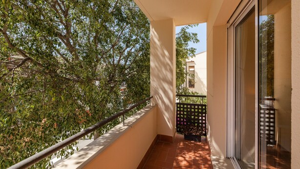 A balcony with a view of trees, a tiled floor, and a glass door.