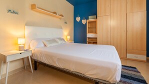 A bedroom with a bed, bedside lamps, a wooden wardrobe, and a shelf above the bed.