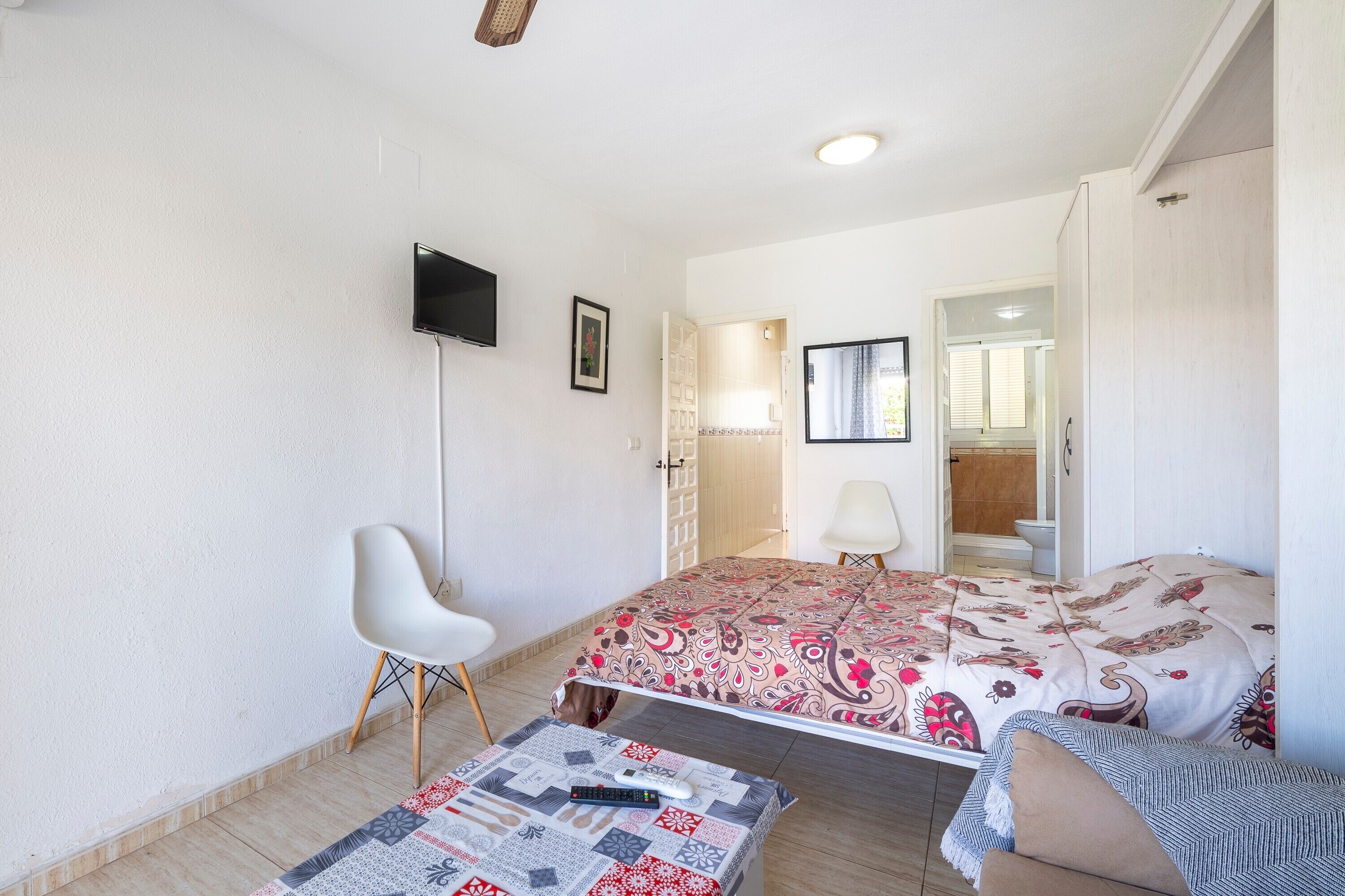 A bedroom with a bed, a chair, a TV, and a bathroom visible through an open door.