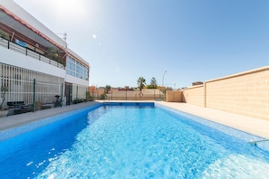 Una piscina con superficie de agua azul cristalina, rodeada por un edificio blanco con techo rojo y un muro de ladrillo.