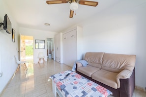 Una sala de estar con un sofá color beige, una mesa con motivos, un ventilador de techo y una puerta que da a un balcón.
