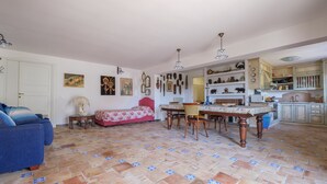A spacious living area with a dining table, a sofa, and a kitchen area with cabinets and shelves.