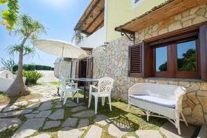 Une terrasse avec un sol en pierre, des meubles en osier blancs et un grand parasol.