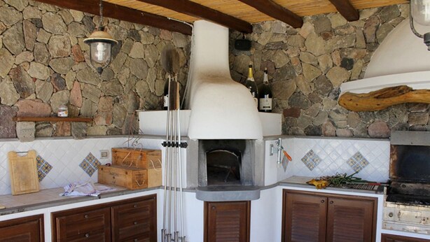 A rustic kitchen with a stone wall, wooden cabinets, and a built-in pizza oven.