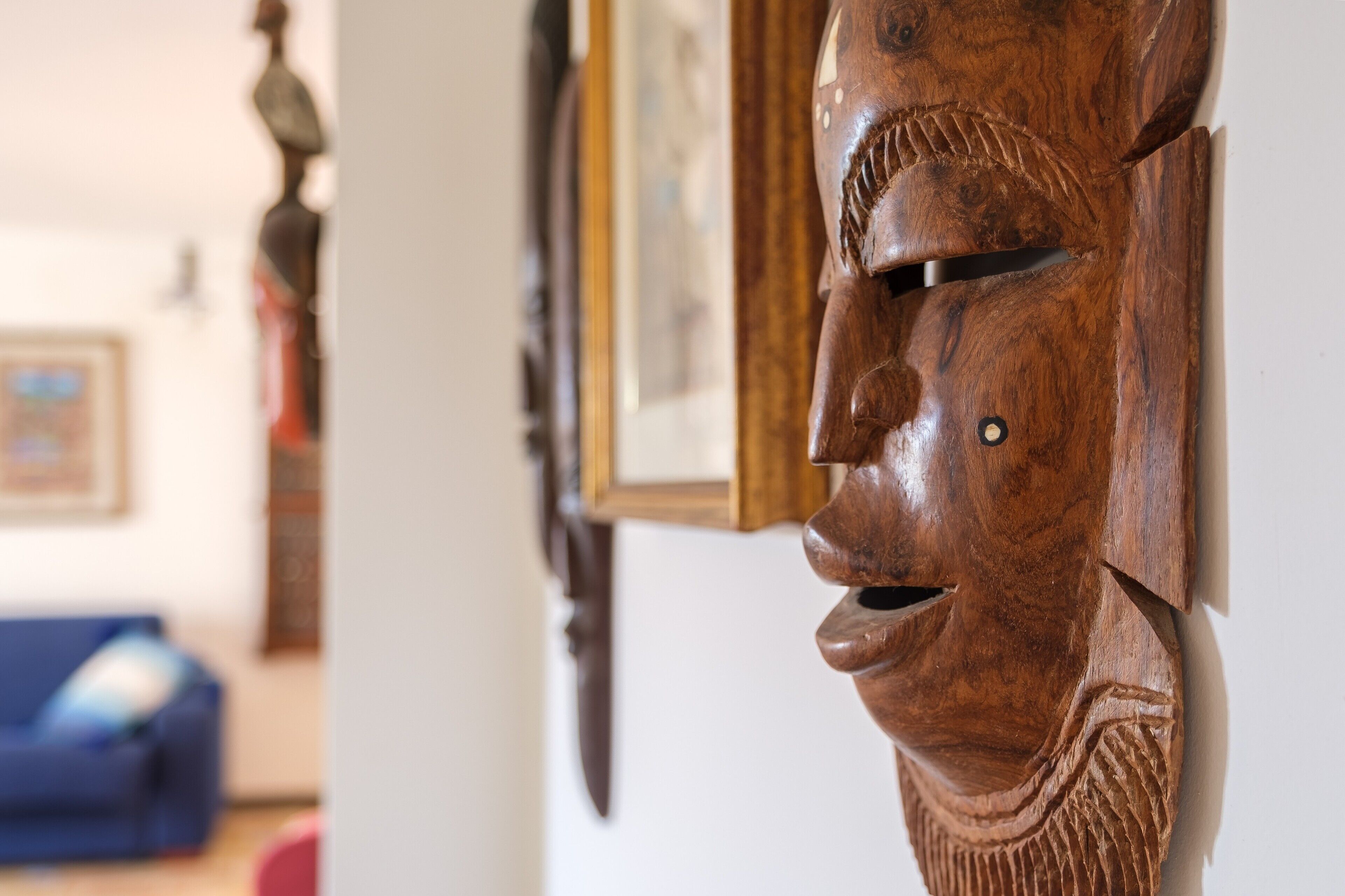Una escultura de madera con rostro tallado, un cuadro en la pared y un sofá azul al fondo.