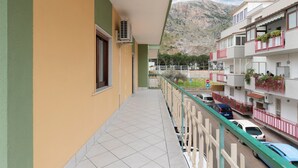 Un balcón con vistas a una montaña, suelo de baldosas y un coche estacionado.