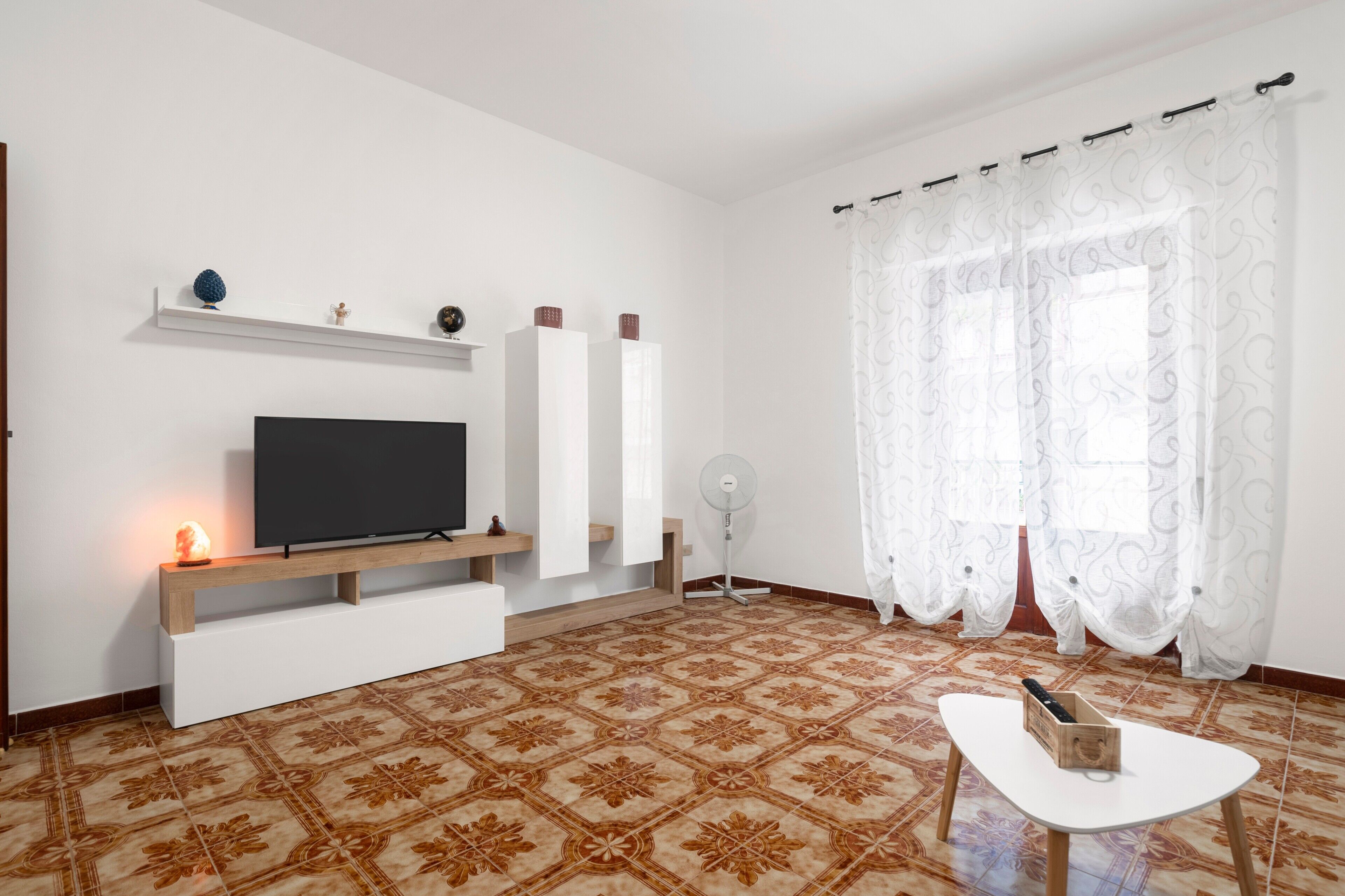 Ein Wohnzimmer mit Flachbildfernseher, einer Holz-Unterhaltungsanlage, einem Standventilator und einem Musterfußboden.