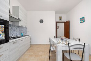 A kitchen with a stove, sink, and patterned backsplash. There is a dining table with chairs and a clock on the wall.