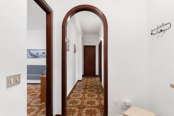 A hallway with patterned flooring, a wooden door at the end, and a wall-mounted light fixture.
