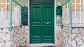 Puertas dobles verdes con un muro de piedra y una barandilla metálica a cada lado.
