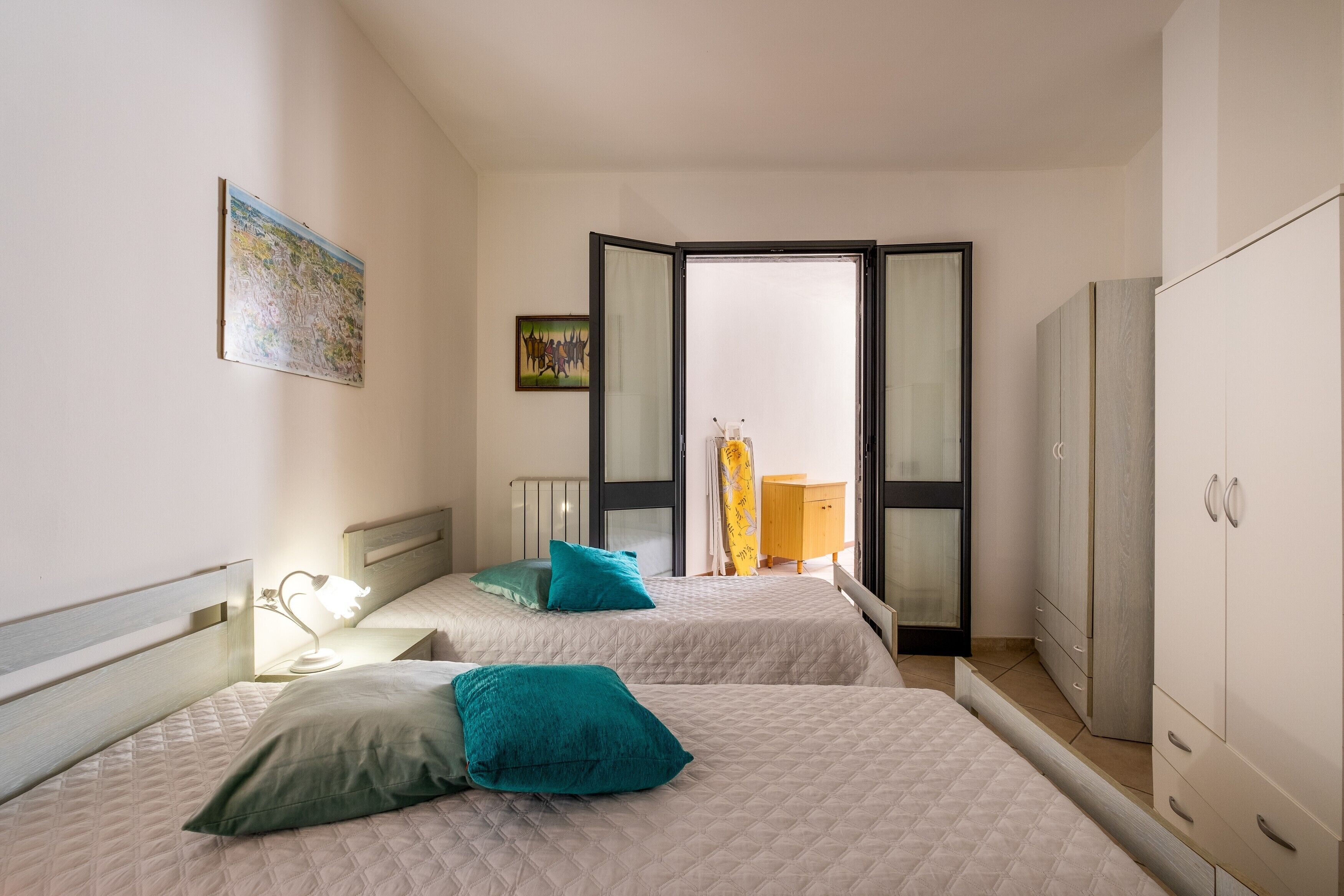 A bedroom with two beds, a wardrobe, a radiator, and a window with curtains.