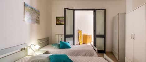 A bedroom with two beds, a wardrobe, a radiator, and a window with curtains.