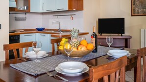 Una mesa de comedor dispuesta con platos, vasos, una botella de vino y un frutero.