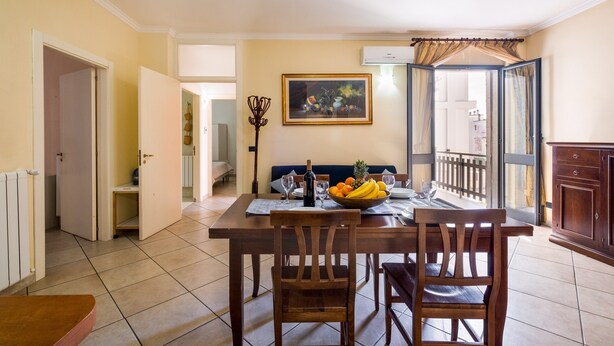 Un comedor con una mesa preparada para dos personas, un frutero y un cuadro en la pared.