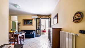 Una sala de estar con comedor, un sofá, una mesa con sillas, un radiador y un objeto decorativo en la pared.