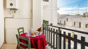 Un balcón con una mesa lista para el desayuno, una pared blanca con calentador de agua y vistas a edificios cercanos.