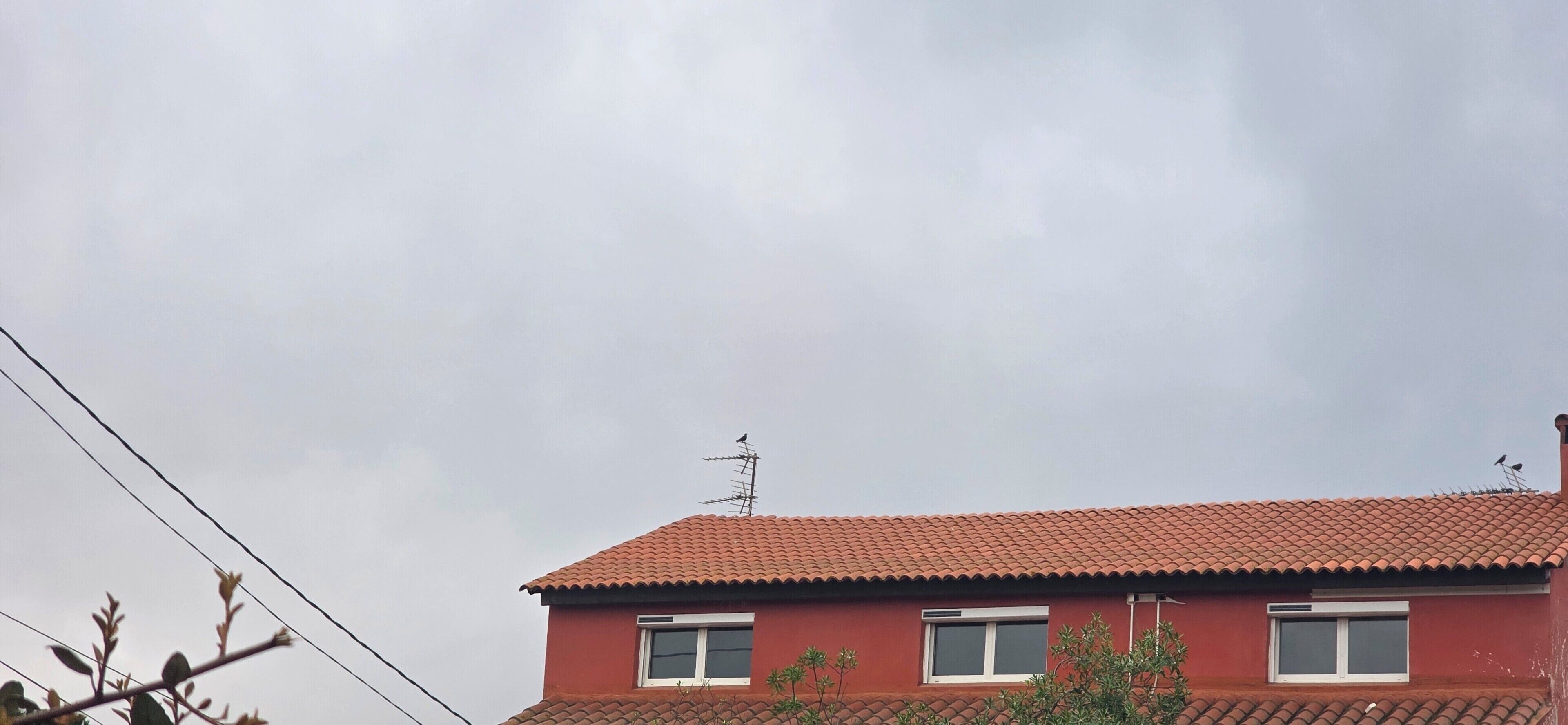 A red-roofed building with three windows and an antenna.
