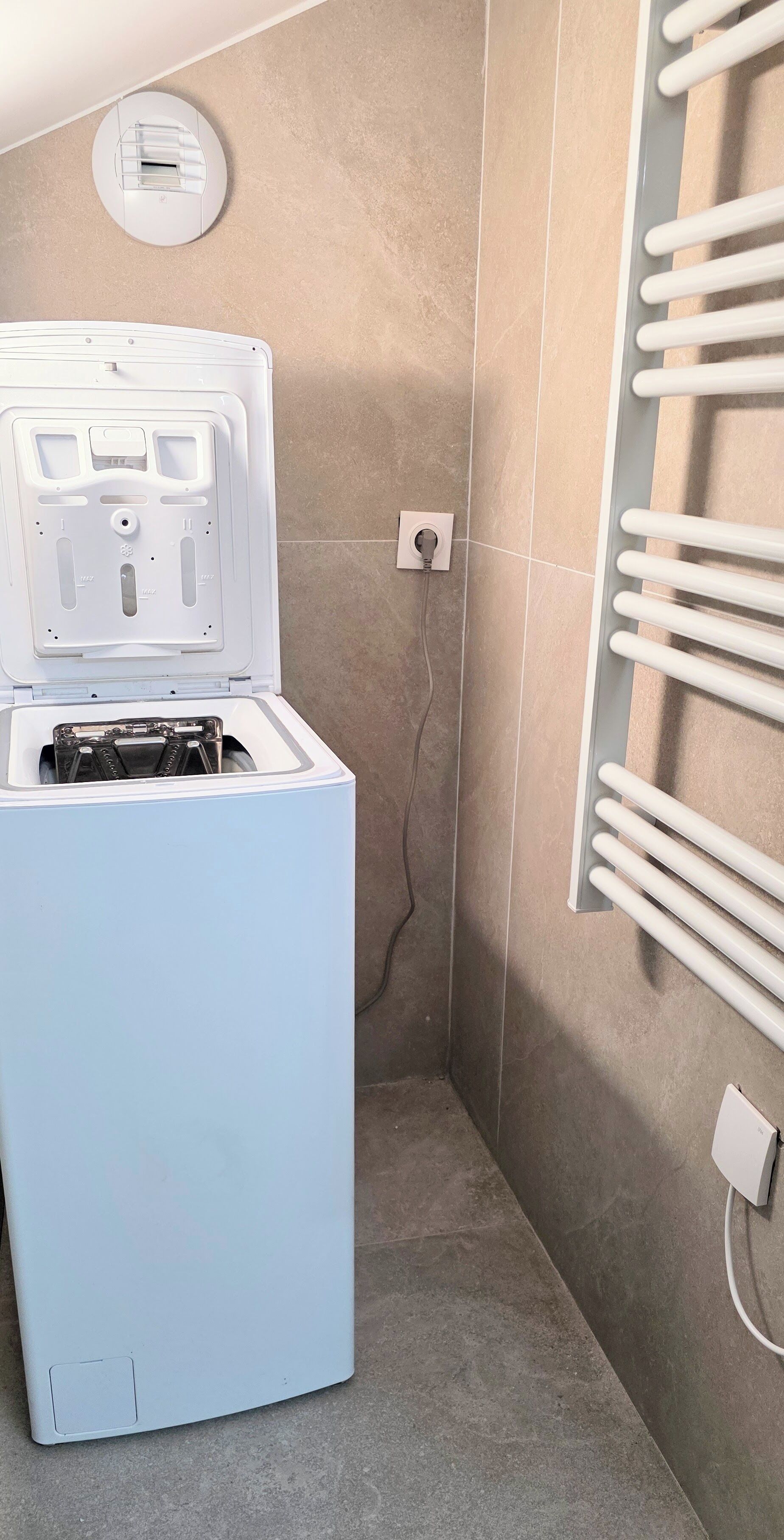 Une petite pièce équipée d’un lave-linge blanc, d’un radiateur fixé au mur et d’une prise de courant.