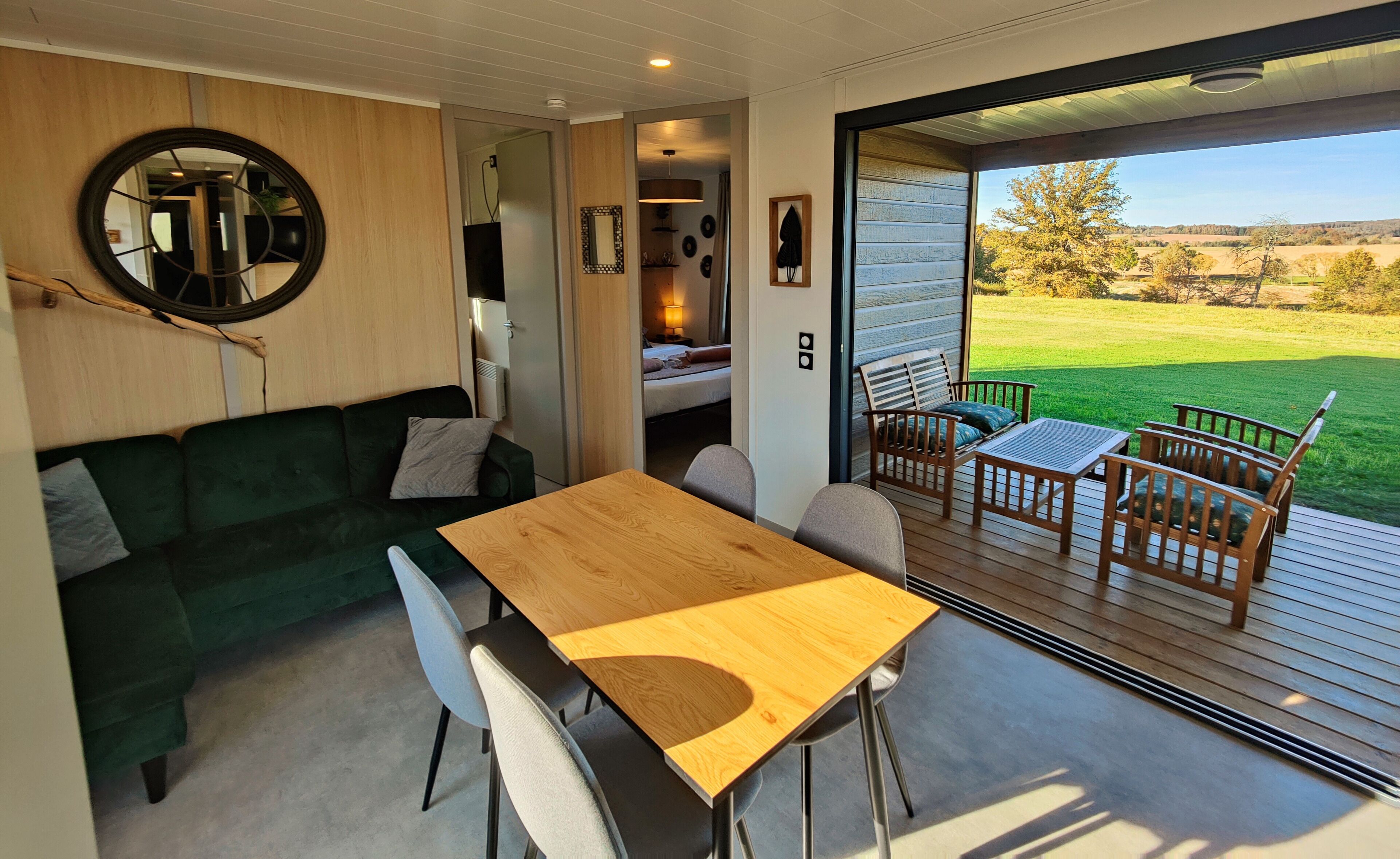 Ein moderner, gut beleuchteter Raum mit einem Holztisch und -stühlen, einem grünen Sofa und einem großen Fenster mit Blick auf ein grünes Feld.