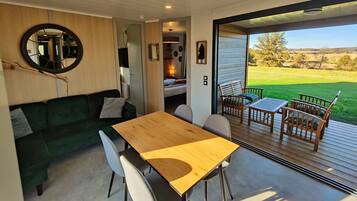 Ein moderner, gut beleuchteter Raum mit einem Holztisch und -stühlen, einem grünen Sofa und einem großen Fenster mit Blick auf ein grünes Feld.