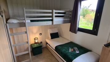 A bunk bed room with a green cushion, a bedside table with a lamp, and a window with a view of greenery.