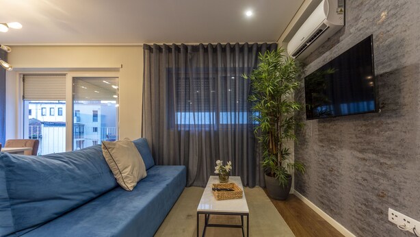 Un salon moderne avec un canapé bleu, une table basse blanche, une plante en pot et un téléviseur fixé au mur, lequel présente une texture particulière.