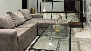 A modern living room with a sectional sofa, a glass coffee table, and a decorative shelf with artwork and sculptures. - Post Ridge Hotel and Restaurant (Kweiman)