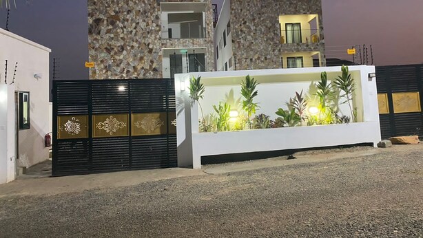 A modern building with a stone facade, a gated entrance, and a landscaped area with plants and a water feature. - Post Ridge Hotel and Restaurant (Kweiman)