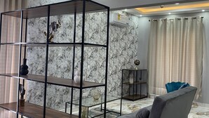 A modern living room with a sectional sofa, a glass and wood shelving unit, marble-patterned walls, and recessed ceiling lighting. - Post Ridge Hotel and Restaurant (Kweiman)