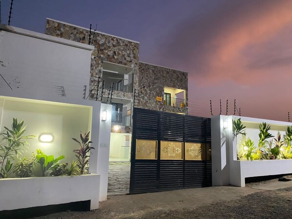 Un bâtiment moderne avec une façade en pierre, un portail noir et des plantes en pot.