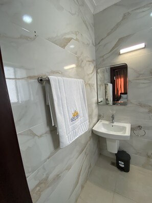 Une salle de bain aux murs recouverts de marbre, avec un lavabo blanc et une serviette suspendue à un porte-serviettes.